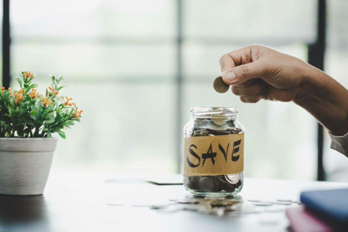 glass jar that says save and a person putting coins inside